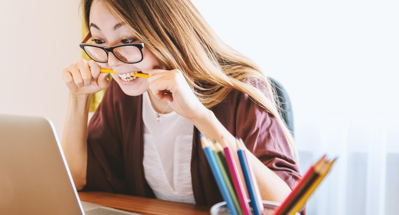 Women biting on pencil stressed while working on laptop